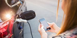 Kvinne som holder telefonen og lader bilen