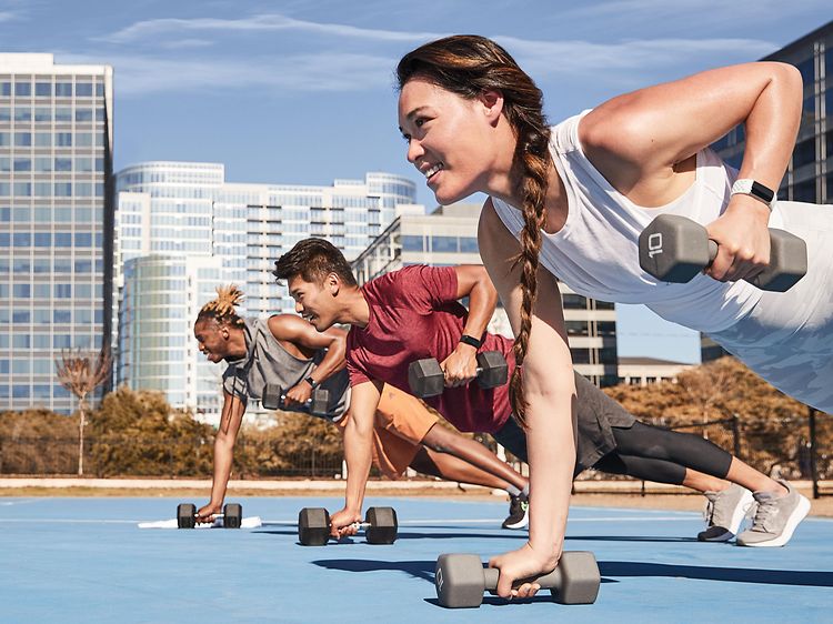 Fitbit Charge 5 på håndleddet til tre personer som trener med manualer