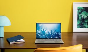 En HP Pavilion 13 på et skrivebord foran en knall gul vegg