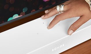 en hånd tar på en Sonos Beam lydplanke