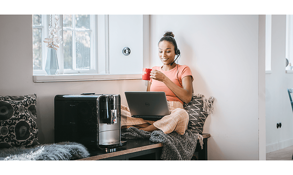 En kvinne med et headset foran bærbar datamaskin ved siden av en kaffemaskin