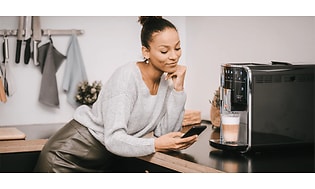En kvinne med en smarttelefon ved siden av en Melitta kaffemaskin