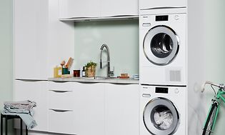 Hvit vaskemaskin og tørketrommel i et vaskerom med hvitt og grønt interiør