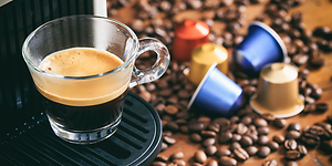 En kopp espresso fra en kapselmaskin med kapsler og kaffebønner på kjøkkenbenk