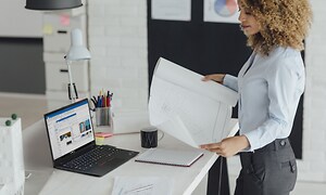 Kvinnelig arkitekt ser på en tegning med Lenovo ThinkPad ved siden av henne på et bord