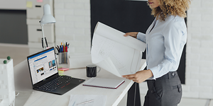 Kvinnelig arkitekt ser på en tegning med Lenovo ThinkPad ved siden av henne på et bord