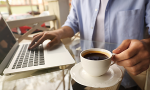 person sitter med en full kaffekopp og jobber på en bærbar pc