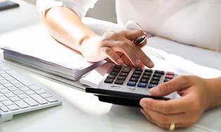 Kvinne med kalkulator i hånded som lener armen på en bunke papir