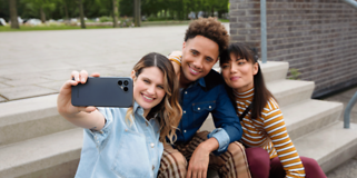 Fairphone 4 i hånden på en kvinne som tar bilde med to andre personer