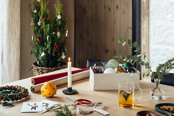 julepynt og innpakning til julegaver på et bord med levende lys og et juletre i bakgrunnen
