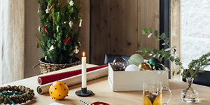julepynt og innpakning til julegaver på et bord med levende lys og et juletre i bakgrunnen