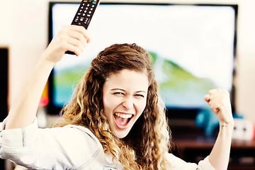 en kvinne jubler stående foran en tv med en fjernkontroll i hånda