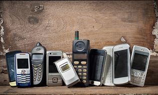 ulike typer eldre mobiltelefoner står ved siden av hverandre mot en trevegg