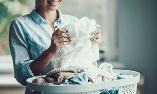kvinne tar ut og bretter klær fra en kurv med klesvask