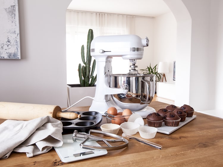 hvit kjøkkenmaskin på et bord ved siden av kjøkkenutstyr, egg og muffins