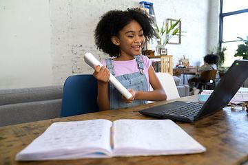 en ung jente gjør skolearbeid på en bærbar pc med en oppslått bok foran seg