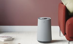En grå Flow A3 som står i et lyst rom ved siden av en rød sofa