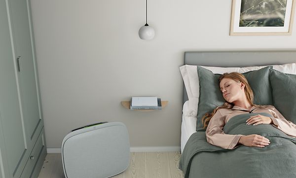 En dame som sover i sengen sin med en grå Well A5 på gulvet ved siden av seg