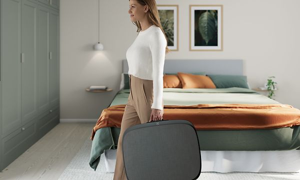 A lady in a living room carrying a big dark grey Well 5 like a suitcase