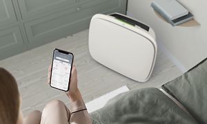 En hvit Well A5 på gulvet og en person med Wellbeing-appen på telefonen