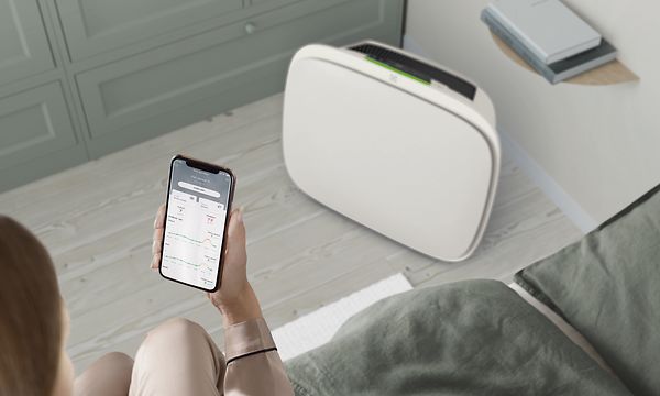 En hvit Well A5 på gulvet og en person med Wellbeing-appen på telefonen