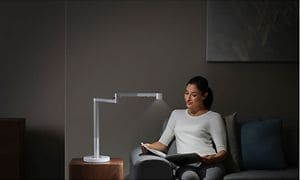 kvinne sitter I en sofa og leser i et blad ved siden av en Dyson-lampe