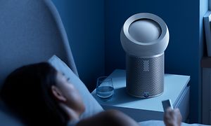 En kvinne ligger i sengen og stiller søvn-timeren på en Dyson Pure Cool Me