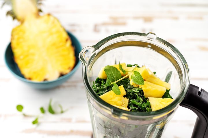 En halv ananas ved siden av en blender med grønt og ananas