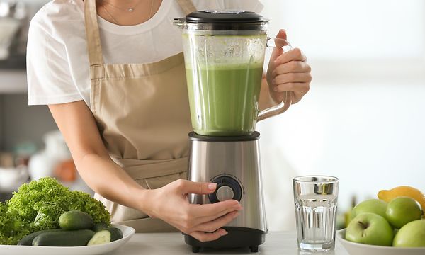 En blender med en grønn smoothie og en kvinne som justerer hastigheten