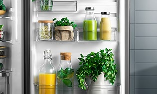 Kjøleskap med appelsinjuice og grølnn smoothie og friske urter i dørhyllen