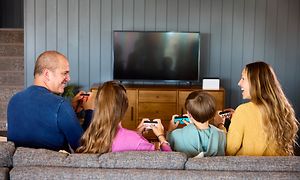 En familie på fire som sitter i en sofa og spiller Nintendo Switch sammen