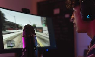 En gamer sitter foran en skjerm og streamer med en blå Yeti X streaming-mikrofon