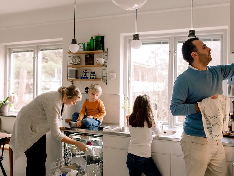 En familie på kjøkkenet tar ut rent servise fra oppvaskmaskinen.