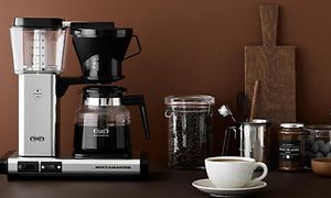 Moccamaster kaffetrakter, kaffekopp og kaffe på bord