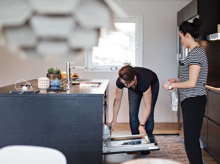 Et par står i et kjøkken og fyller opp en integrert oppvaskmaskin
