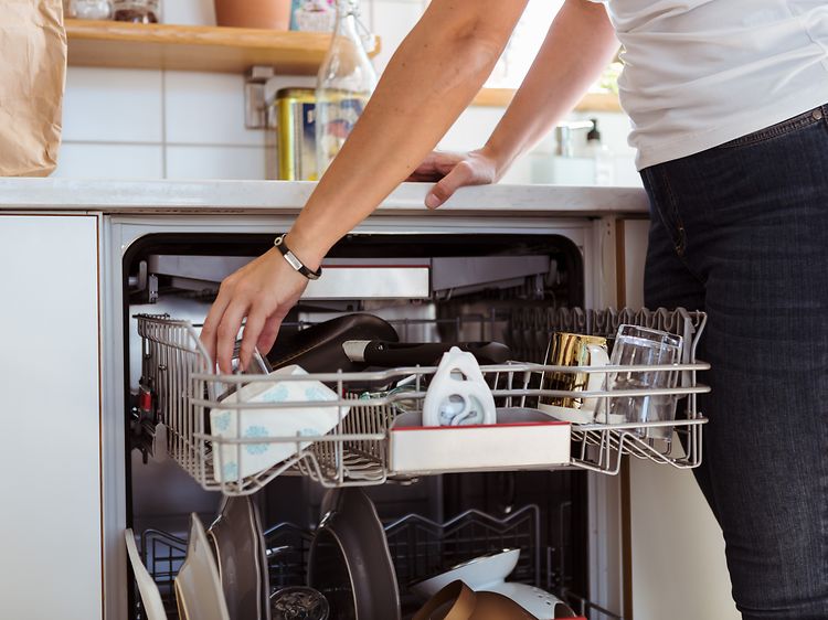 En kvinne lener seg over kjøkkenbenken og tømmer oppvaskmaskinen