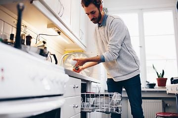 En mann skyller en kopp i vasken ved siden av en oppvaskmaskin