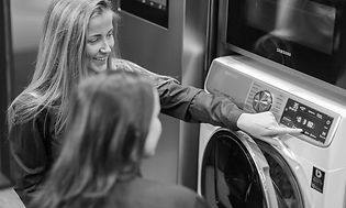Smilende kvinne som viser en annen kvinne en vaskemaskin