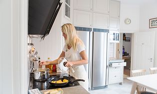 En kvinne lager mat på kjøkkenet med et kjøleskap og fryser i bakgrunnen