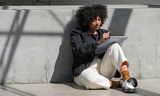 Kvinne sitter mot betongveggog bruker en bærbar datamaskin som et nettbrett