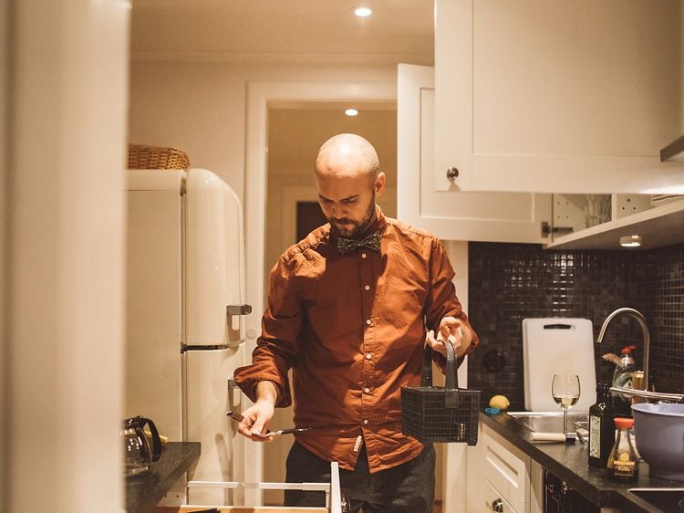 En mann holder en bestikkurv på kjøkkenet
