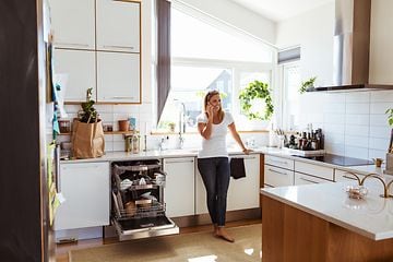 En kvinne snakker i telefonen mens hun står i et kjøkken med en åpen, integrert oppvaskmaskin