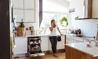 En kvinne snakker i telefonen mens hun står i et kjøkken med en åpen, integrert oppvaskmaskin