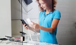 En ung kvinne holder opp og sammenligner smarttelefoner i en butikk