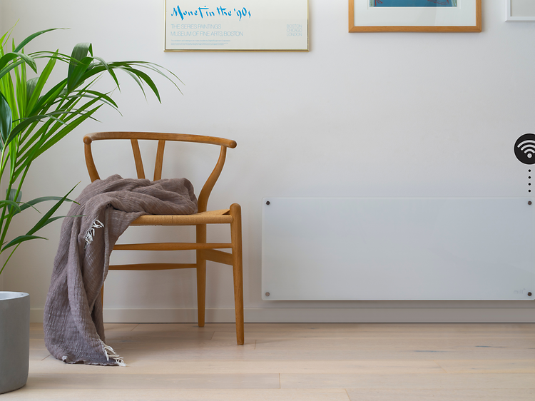 Smart panelovn på vegg med wifi-symbol og trestol og plante i front