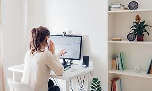 kvinne jobber hjemmefra foran skrivebord med pc-skjerm mens hun snakker i telefonen