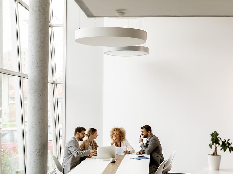 fire mennesker sitter rundt et bord i et hvitt rom og jobber sammen