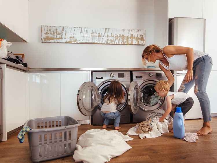 En kvinne og to barn laster inn klær i en vaskemaskin på et vaskerom
