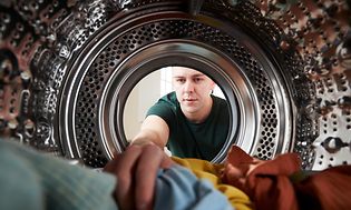 En mann laster klær inn i vaskemaskinen