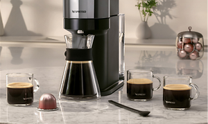 Nespresso Vertuo kaffemaskin og kaffekopper med kaffe ved siden av